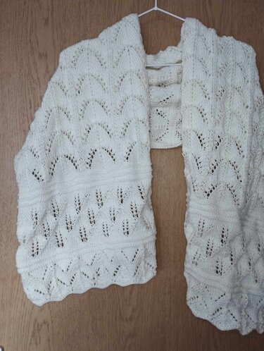 Weißes gestricktes Stola-Tuch mit Spitzen- und Blattmotiv, aufgehängt an einem Bügel