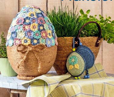 Großes Deko-Ei mit einer Haube aus bunten Häkelblüten und Schnur-Umwicklung, umgeben von Kräutern und kleinen gehäkelten Eiern