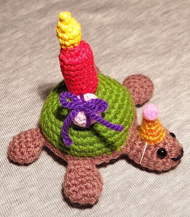 Gehäkelte Schildkröte mit Geburtstagskerze und Partyhut auf neutralem Hintergrund