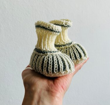 Gestrickte Babyschuhe in Creme mit grauen Streifen, Detailaufnahme in einer Hand
