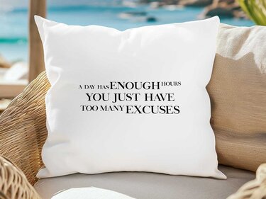 Weißes Kissen mit dem englischen Spruch „A Day Has Enough Hours You Just Have Too Many Excuses“ auf einem geflochtenen Sessel vor Strandkulisse