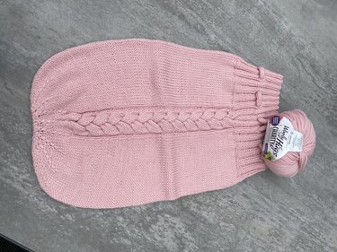 rosa gestrickter Babysack mit mittigem Zopfmuster und Knäuel auf hellem Untergrund