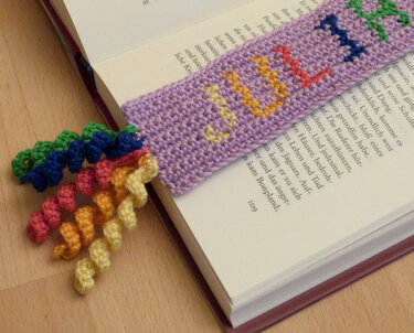 Gehäkeltes lila Lesezeichen mit LOVE‑Schrift und bunten Spiralen in einem aufgeschlagenen Buch