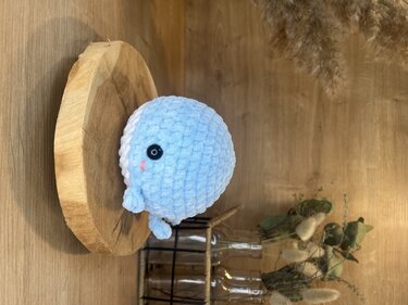 Gehäkelter blauer Amigurumi-Wal auf runder Holzscheibe