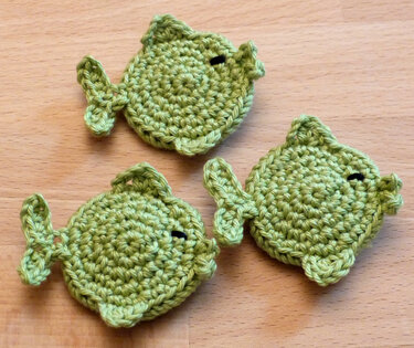 Drei runde gehäkelte Fische in Grün, dekorativ angeordnet