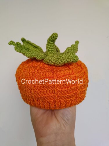 Orange crocheted amigurumi pumpkin with green leaves held in a hand