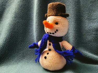 Gehäkelter Amigurumi-Schneemann mit braunem Zylinderhut, blauem Schal und Karottennase