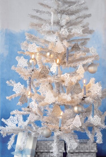 Weißer Weihnachtsbaum mit gehäkelten Sternen, silbernen Kugeln und Kerzen