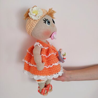 Crocheted amigurumi doll in an orange tiered dress with flower headband and pink pacifier