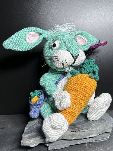 Gehäkelter mintgrüner Amigurumi-Hase mit großer oranger Karotte und kleinem blauen Täschchen