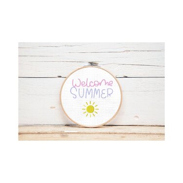 Runder Stickrahmen mit besticktem Text 'Welcome SUMMER' in Pastellfarben und gelber Sonne vor hellem Holz