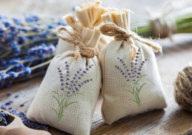 Zwei bestickte Stoffbeutel mit Lavendelmotiv, getrockneter Lavendel und Holzlöffel auf Holzoberfläche