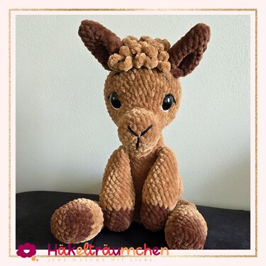 Gehäkeltes braunes Lama Amigurumi mit dunklen Ohren und Pfoten, sitzend.