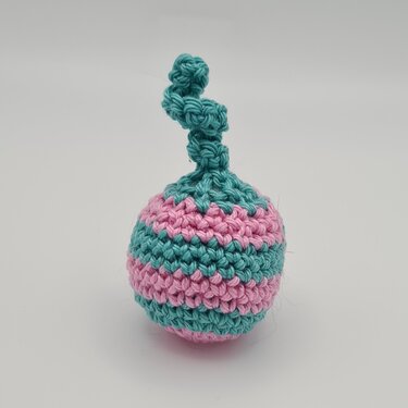 kleine gehäkelte Katzen-Spielkugel mit rosa und türkis gestreiftem Muster und gedrehter Schlaufe oben