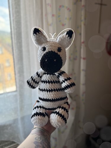 Hand hält gehäkeltes Zebra-Amigurumi in schwarz-weiß mit gestreifter Körpermusterung und dunkler Schnauze