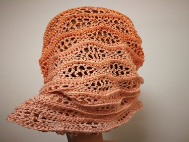 Nahaufnahme eines gehäkelten Loop-Schals in Orange- und Pfirsichtönen auf einer Schaufensterpuppe mit offenem Wellenmuster.