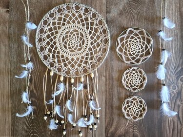 Beiger gehäkelter Traumfänger mit Holzperlen und weißen Federn neben drei kleinen gehäkelten Mandalas auf Holzhintergrund
