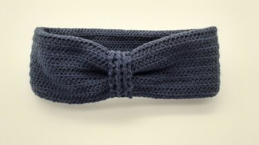 Nahaufnahme eines dunkelblauen, gehäkelten Stirnbands mit verdrehtem Knoten in der Mitte.