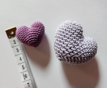 Nahaufnahme: zwei gehäkelte Amigurumi‑Herzen neben einem Maßband