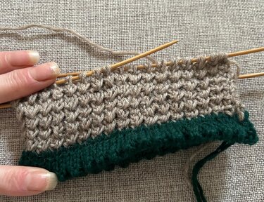 Nahaufnahme einer Strickprobe für Sockenbündchen in Beige und Grün, gestrickt im Perlmuster und Rippenbündchen auf Nadelspiel.