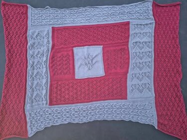 Gestrickte Patchwork-Decke in Koralle und Hellgrau, flach ausgelegt mit Loch-, Zopf- und Strukturmustern.