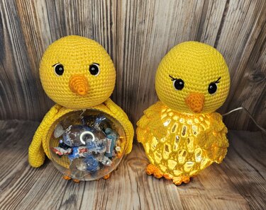 Zwei gelbe, gehäkelte Küken, eines als Süßigkeitenbehälter, das andere als Lichtobjekt, auf Holzuntergrund.