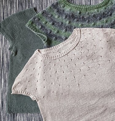 Three women's short-sleeve knit tops laid flat: cream eyelet top, solid sage tee, green variegated yoke sweater