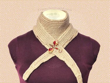 Schmales cremefarbenes gestricktes Dreieckstuch, gekreuzt am Hals einer Büste, mit rot-goldener Drachenbrosche.