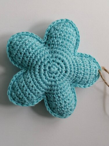 Nahaufnahme einer türkisen gehäkelten Blume mit fünf Blütenblättern und Befestigungskordel auf hellem Hintergrund