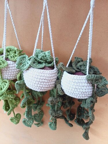 Three white crocheted hanging planters with green heart-shaped trailing vines against a neutral background.