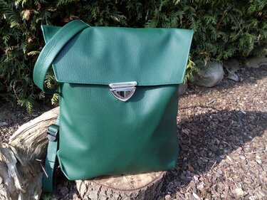 Grüner genarbter Kunstleder-Rucksack mit Umschlagklappe und silbernem Verschluss auf Baumstumpf