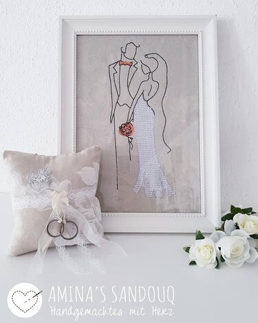 Einfache Linienstickerei eines Brautpaares im Rahmen, mit Ringkissen und Rosen