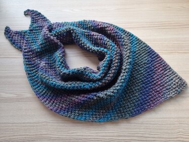 Gestricktes Dreieckstuch in melierten Blau-, Lila- und Grautönen auf hellem Holz