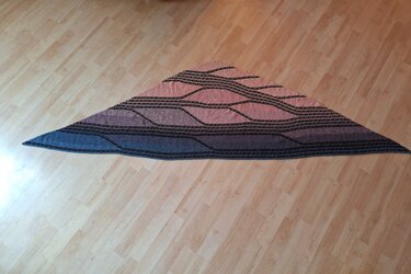 Gestricktes Dreieckstuch mit blau-rosa Farbverlauf und schwarzen Wellenlinien auf hellem Boden