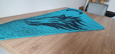 Turquoise garter-stitch triangular shawl with black horse silhouette motif laid flat on a wooden table