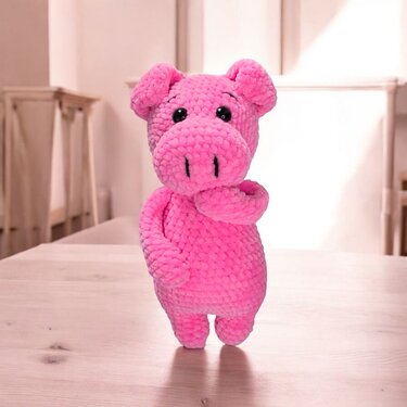 Rosa gehäkeltes Amigurumi-Schwein mit schwarzen Kunststoffaugen, steht auf einem Holztisch
