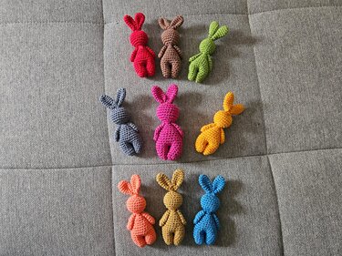 Neun gehäkelte Amigurumi-Hasen in bunten Garnfarben auf grauem Stoff