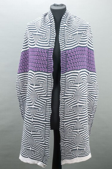Knitted black-and-white geometric shawl with a textured purple band draped over a black dress form