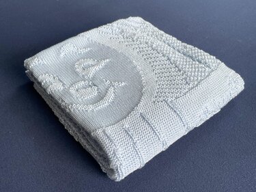 Folded pale blue knitted baby blanket with ribbed edge and raised stitch pattern
