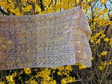 Gehäkelter Schal in hellem Ton mit filigranem Lochmuster vor gelben Blüten