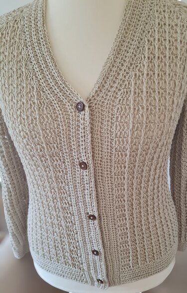 Beige gehäkelte Damenjacke mit V‑Ausschnitt und braunen Knöpfen auf Schneiderbüste