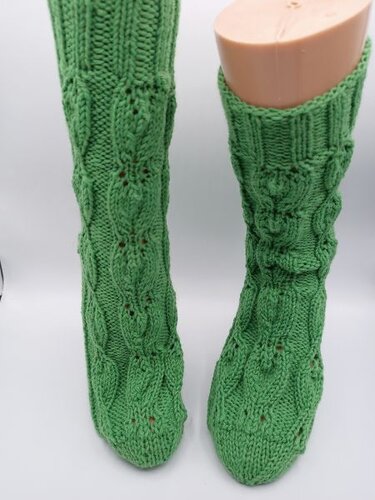 Grüne gestrickte Socken mit Zopfmuster und Lochmuster auf Schaufensterfuß