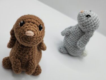 Two cozy crochet bunnies, brown at left and grey at right, standing on a white background