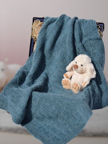 Gestrickte blaue Babydecke mit dezentem Strukturmuster neben einem hellen Plüschtier in einer Holzkiste