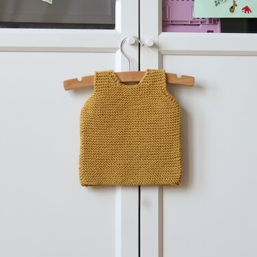 Mustard yellow garter-stitch baby vest on wooden hanger against white cabinet