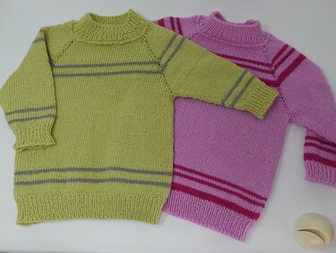 Zwei gestrickte Kinderpullover: lindgrün mit grauen Streifen und rosa mit magentafarbenen Streifen