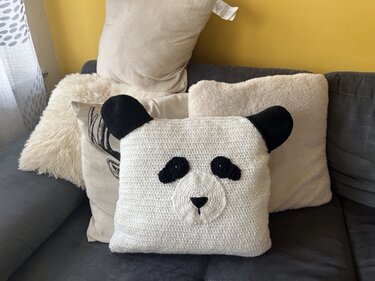 Quadratischer weißer gehäkelter Kissenbezug mit schwarzem Panda-Gesicht auf Sofa