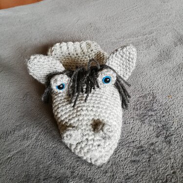 Gehäkelte Pferde-Handpuppe mit blauen Augen und dunkler Mähne auf grauem Untergrund