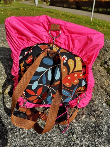 Rucksack mit pinker Regenhülle und floralem Muster auf Felsen