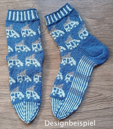 Paar blauer, gestrickter Socken mit weißem Auto-Muster und gestreifter Sohle auf Holz; Schriftzug ‚Designbeispiel‘